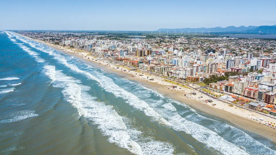 Foto aérea da praia de Capão da Canoa, com o mar de ondas e a orla da cidade